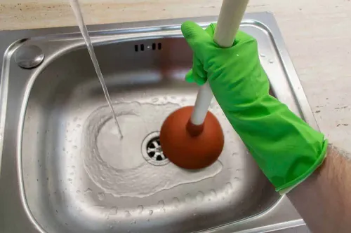 Main avec gants en caoutchouc qui débouche un évier avec une ventouse